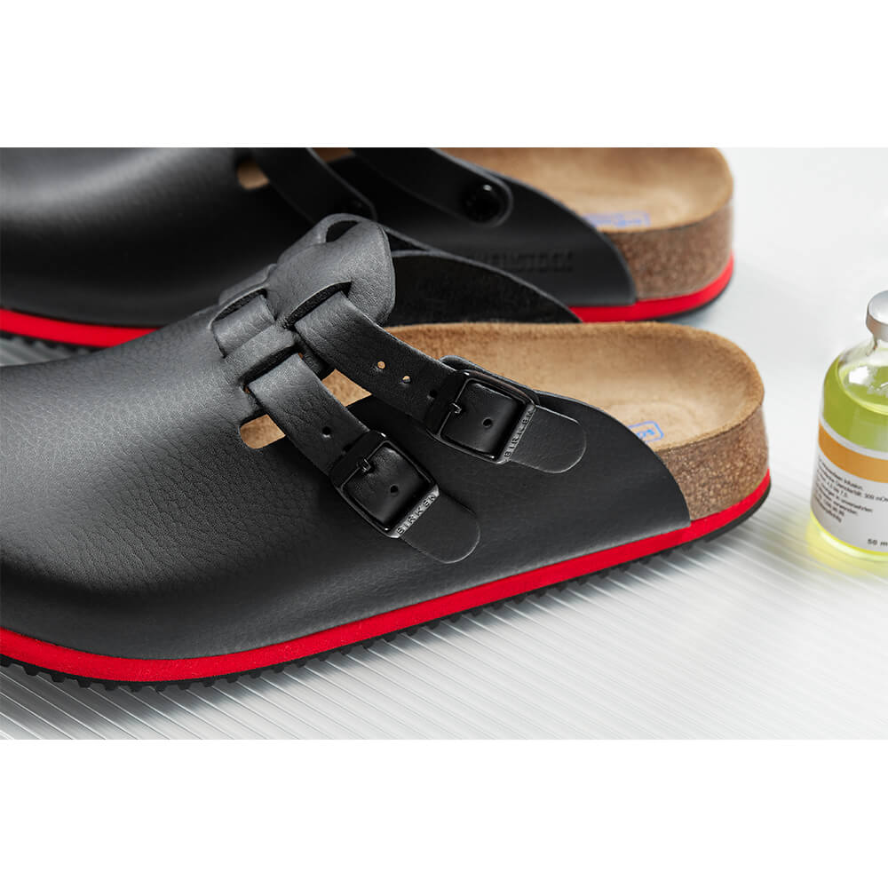 Nahaufnahme schwarzer Clog mit zwei Riemen und Schnallen auf roter Sohle