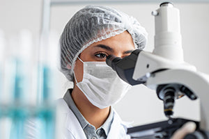 Testo alternativo: donna con mascherina che guarda al microscopio